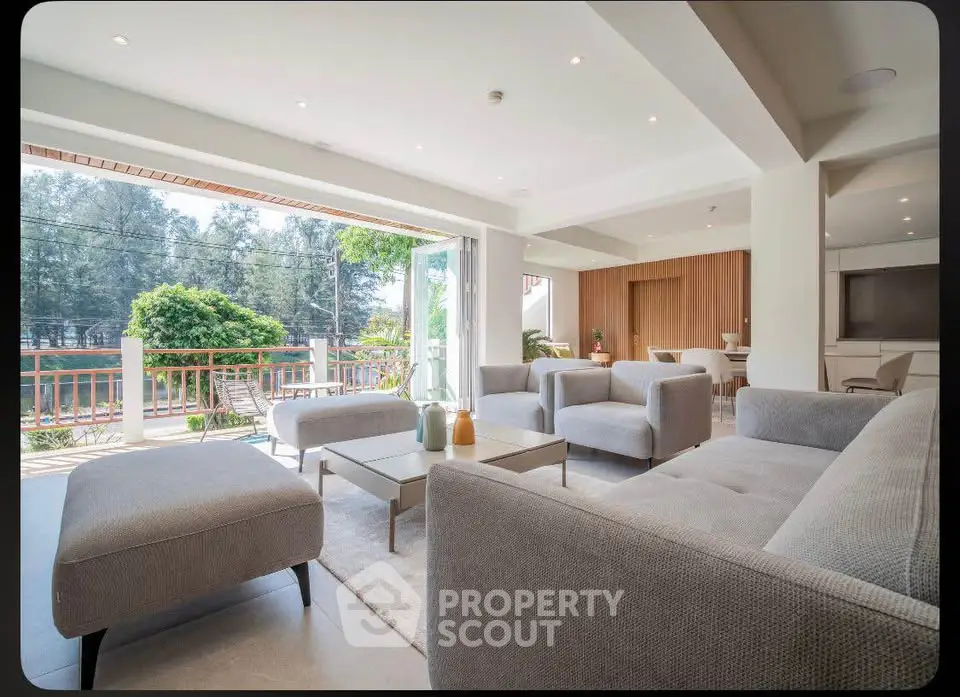 Spacious modern living room with large windows and stylish furniture, offering a serene view of lush greenery.