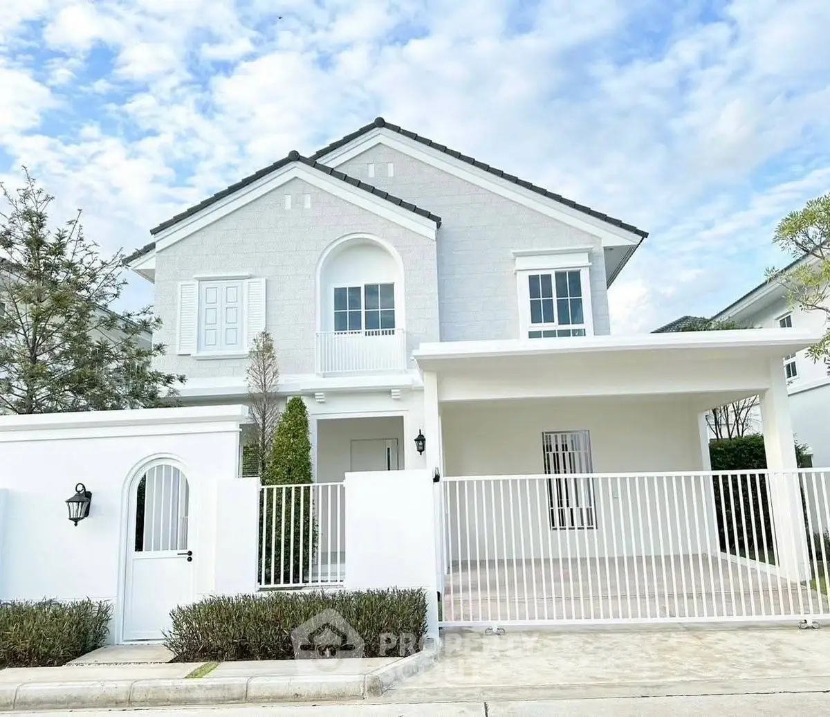 Charming white two-story house with gated driveway and lush greenery