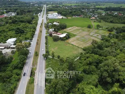 Aerial view of lush green landscape with road and fields, ideal for real estate development.