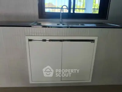 Modern kitchen with sleek cabinetry and stainless steel sink under a large window.