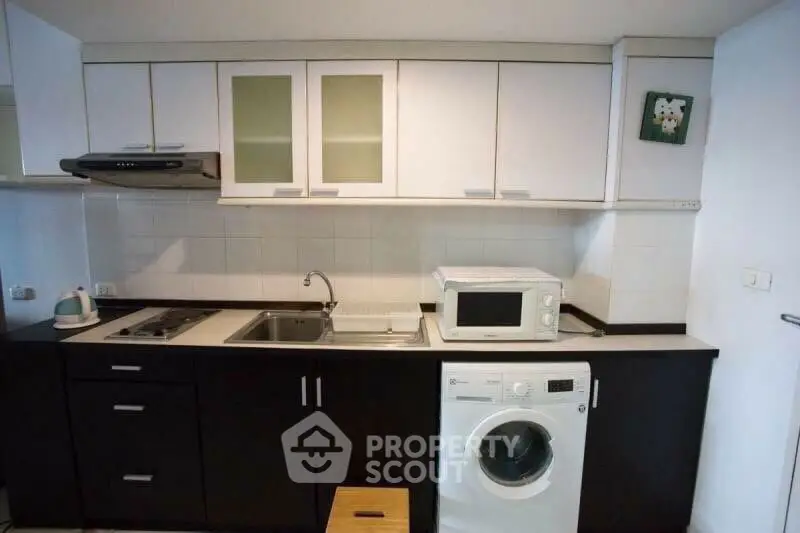 Modern kitchen with sleek cabinets, washing machine, and microwave, perfect for urban living.