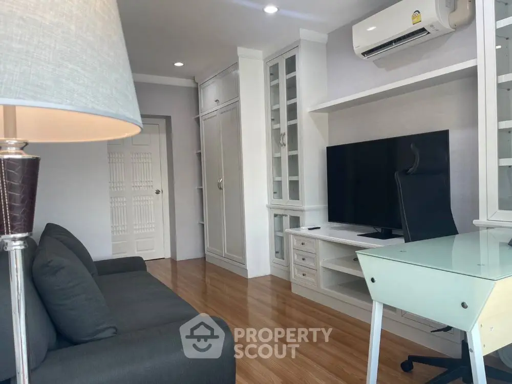 Modern living room with sleek furniture and large TV, featuring wooden flooring and ample natural light.