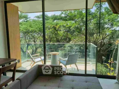 Serene living room with large glass doors opening to a lush balcony view, modern furniture, and abundant natural light.
