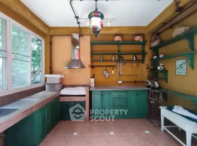 Charming rustic kitchen with green cabinetry and open shelving, featuring a vintage-style light fixture and large windows.