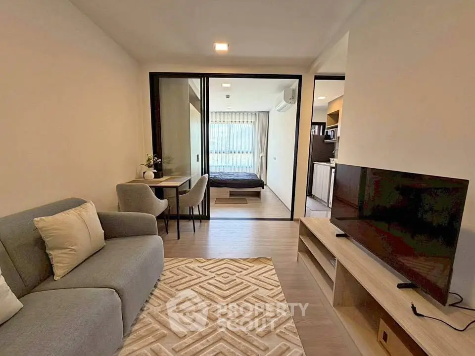 Modern open-plan living room with cozy sofa and TV, leading to a bedroom with natural light.