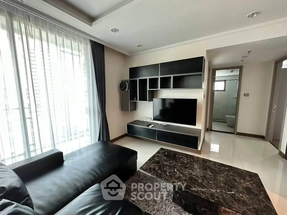 Modern living room with sleek black furniture and wall-mounted TV, featuring large windows for natural light.