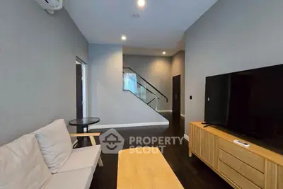Modern living room with sleek furniture and large TV, featuring a stylish staircase and ambient lighting.