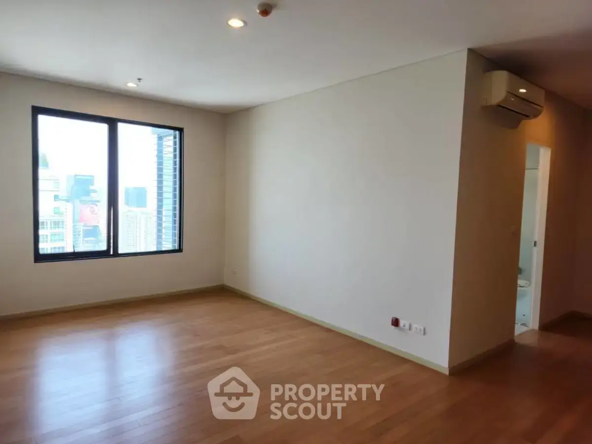 Spacious empty living room with wooden flooring and city view window.