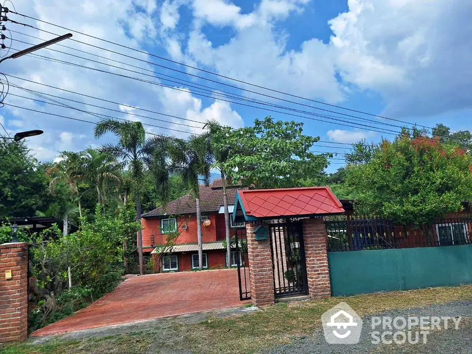 Charming brick house with lush greenery and gated entrance under a vibrant blue sky.