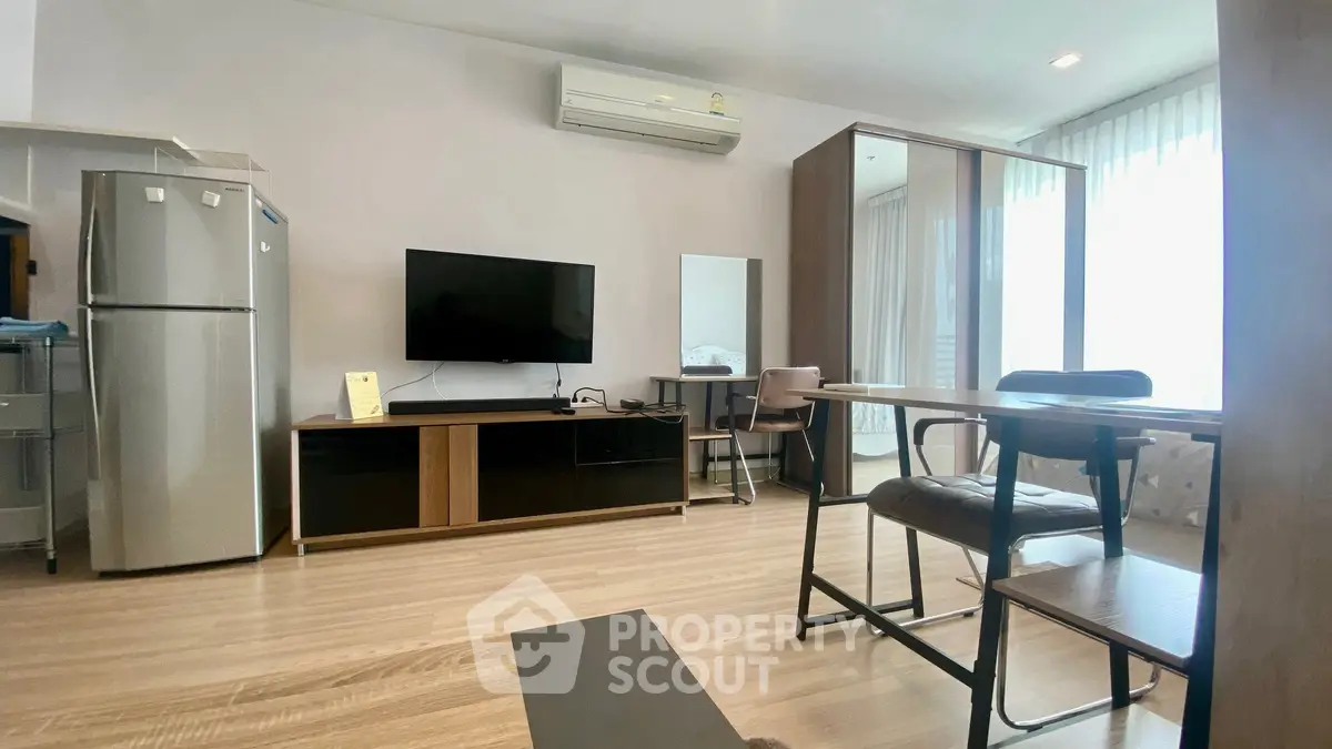 Modern living room with sleek furniture and natural light, featuring a TV and air conditioning.
