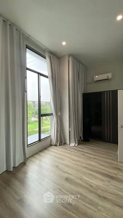 Spacious bedroom with large windows and elegant curtains, offering a serene view of greenery.