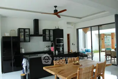 Modern open-layout kitchen with sleek black cabinets and wooden dining table, leading to a bright outdoor patio.
