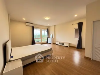 Spacious bedroom with large windows and wooden flooring, offering a serene view.