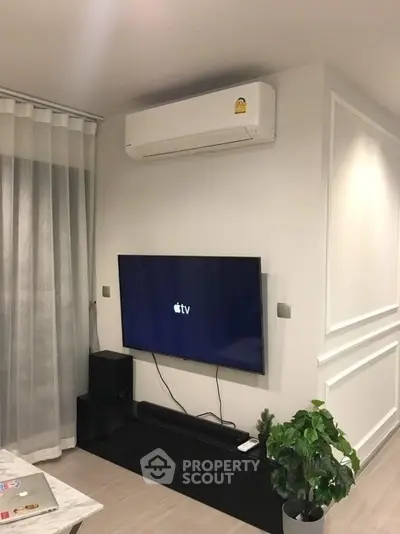 Modern living room with wall-mounted TV and air conditioning unit, sleek decor and potted plant.