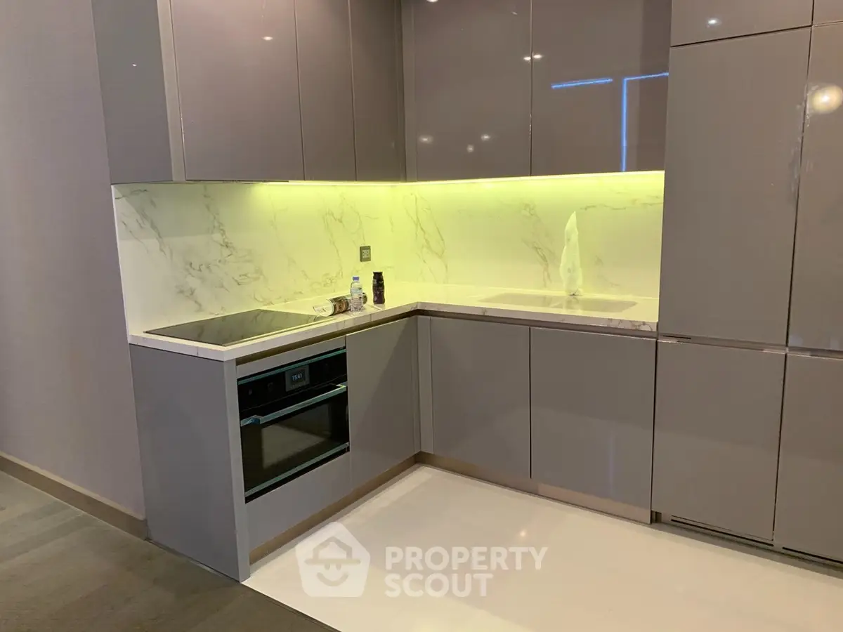 Modern kitchen with sleek cabinetry and built-in oven, featuring elegant marble backsplash and under-cabinet lighting.