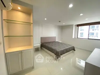 Spacious modern bedroom with large window and built-in shelving in a bright apartment.