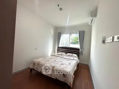 Cozy bedroom with wooden flooring and natural light, featuring air conditioning and a comfortable bed.