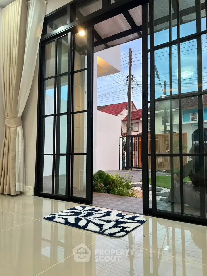 Modern living room with large glass doors opening to a serene garden view, featuring elegant curtains and glossy tiles.