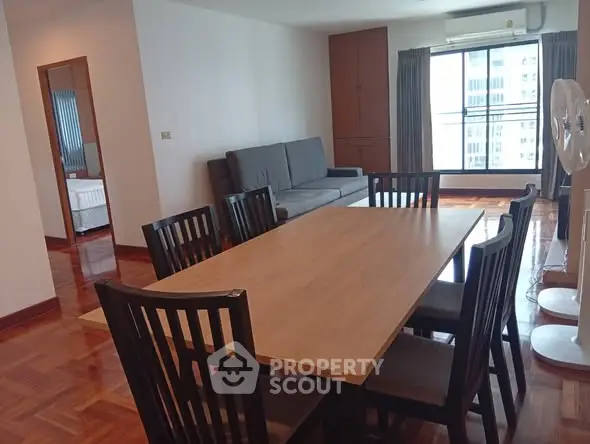 Spacious dining area with wooden table and chairs, adjacent to a cozy living room with a sofa and large window view.