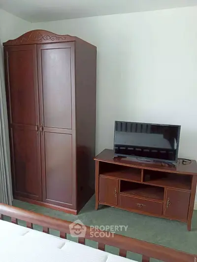 Cozy bedroom with wooden wardrobe and TV stand, perfect for relaxation.