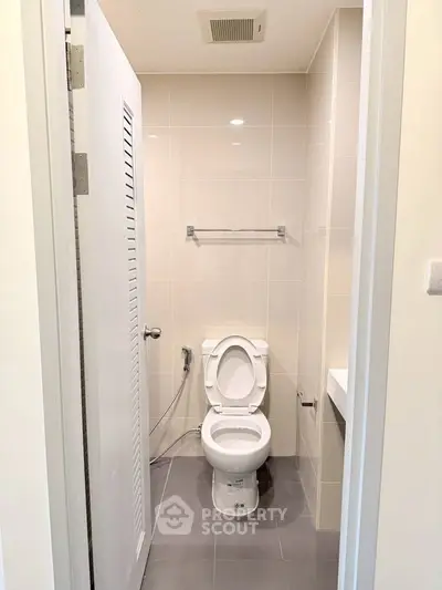 Modern bathroom with sleek design and neutral tones, featuring a toilet and towel rack.