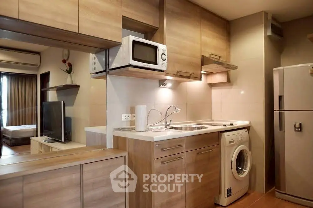 Modern kitchen with wooden cabinets, microwave, and washing machine in cozy apartment.