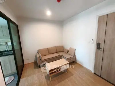Cozy living room with modern sofa and wooden flooring, adjacent to a sleek kitchen area.