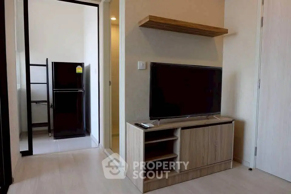 Modern living room with sleek TV stand and wall-mounted shelf, adjacent to a compact kitchen area.