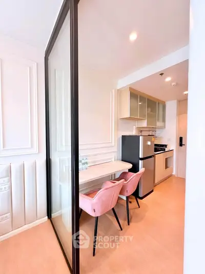 Modern kitchen with dining area featuring pink chairs and glass partition, compact yet stylish design.
