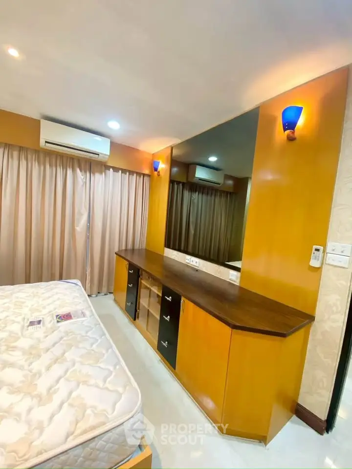 Spacious bedroom with modern wooden furniture and ambient lighting, featuring a large mirror and air conditioning.