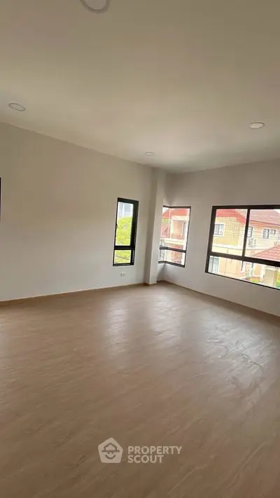 Spacious empty room with large windows and wooden flooring, perfect for customization.