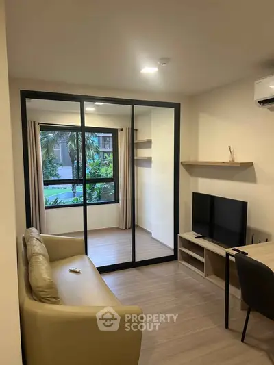 Modern living room with glass partition and garden view, featuring sleek furniture and natural light.