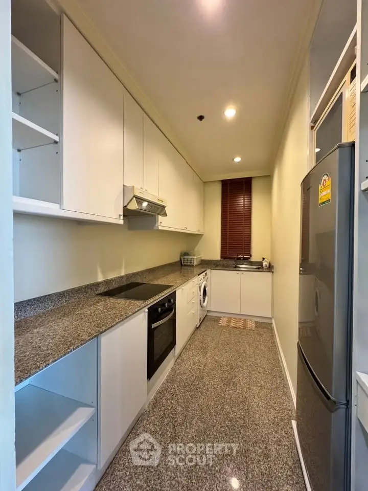 Modern kitchen with granite countertops, built-in oven, and washing machine in sleek apartment.