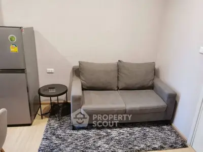 Cozy living room with gray sofa and modern fridge in a compact apartment.