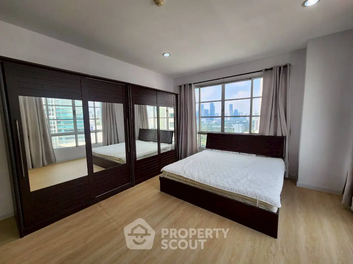 Spacious bedroom with city view, featuring large mirrored wardrobe and wooden flooring.