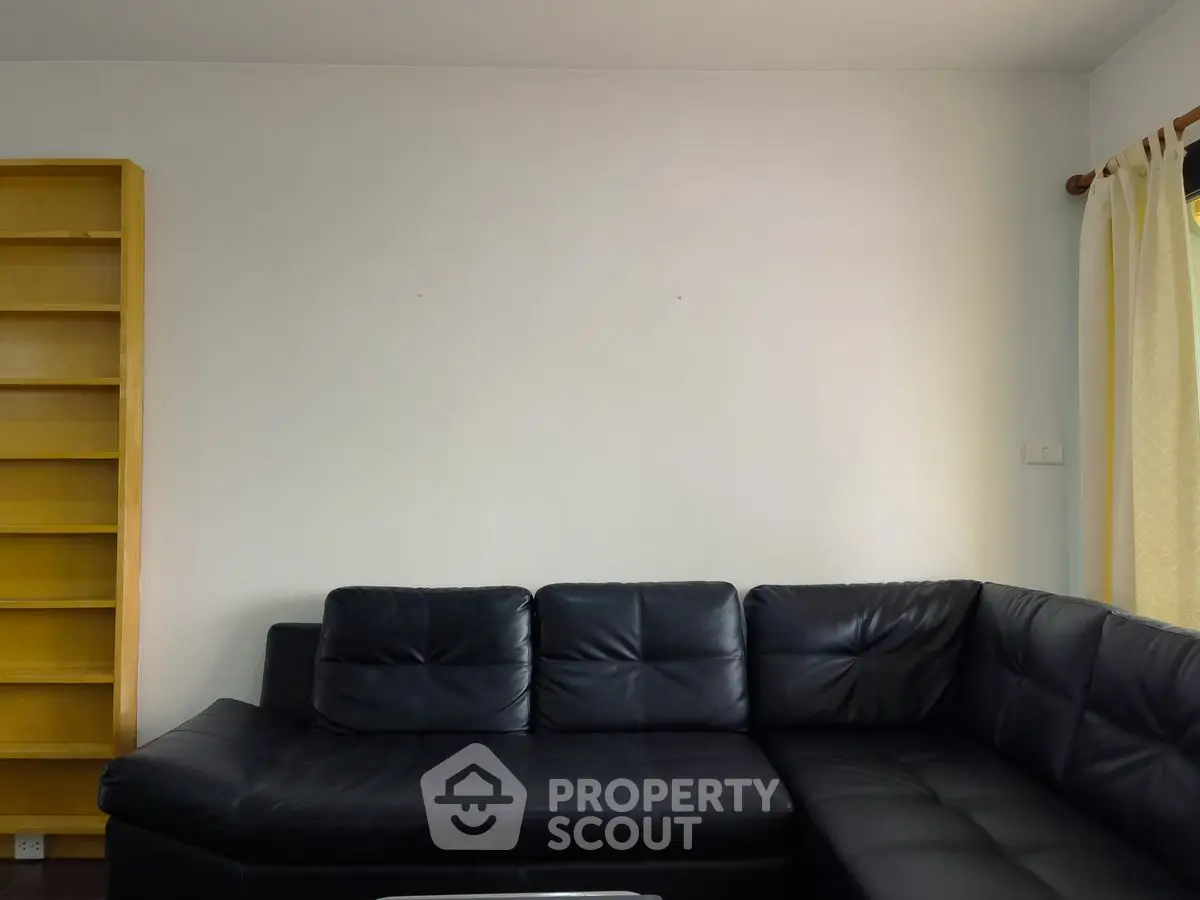 Spacious living room with black leather sectional sofa and wooden bookshelf.