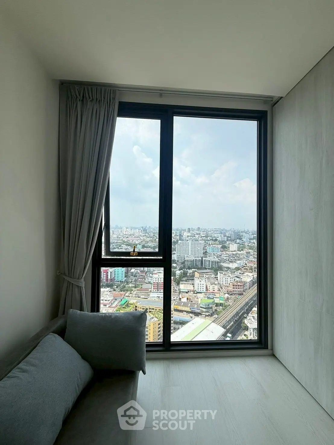 Modern living room with panoramic city view from large window, featuring sleek design and cozy seating.