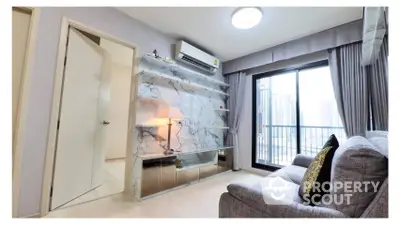 Elegant living room with plush grey sofa, chic marble wall, modern lighting, and access to a sunlit balcony offering an urban view.