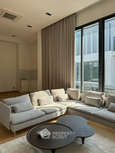 Spacious modern living room with large windows and elegant sectional sofa.