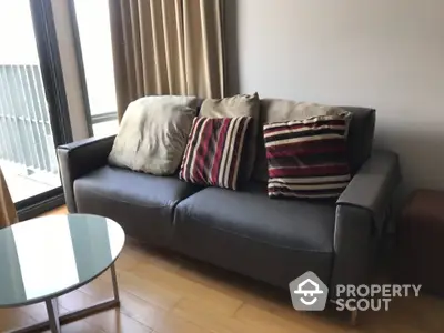 Modern living room with stylish sofa and glass coffee table near large window.