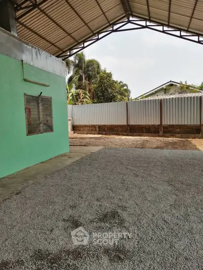 Spacious outdoor area with gravel and green building, ideal for versatile use.