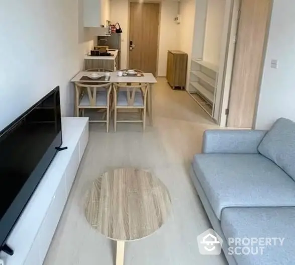 Modern minimalist living room with sleek grey sofa and wooden dining set, complemented by a chic round coffee table and ample natural light.