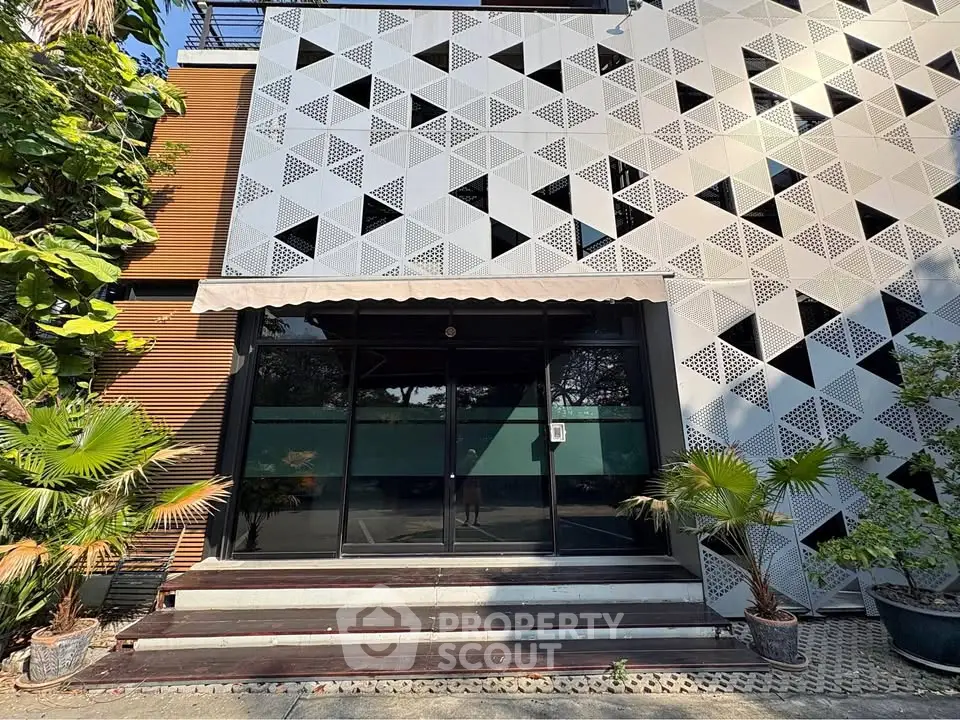 Modern building entrance with geometric facade and lush greenery