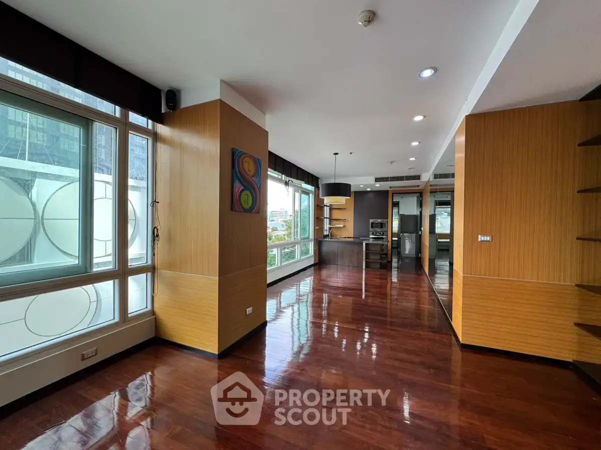 Spacious modern living room with wooden flooring and large windows offering city views.
