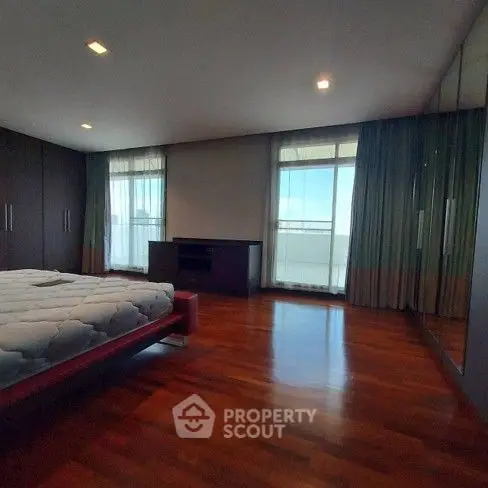 Spacious bedroom with wooden flooring and large windows offering natural light.