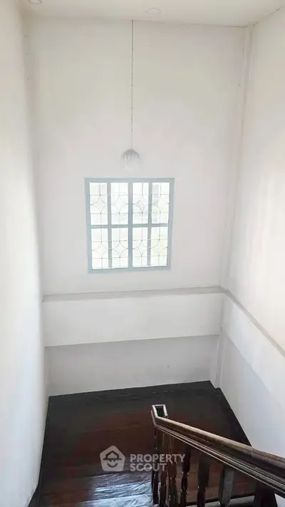 Bright stairwell with wooden steps and a large window, offering natural light and a spacious feel.
