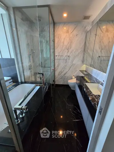 Luxurious modern bathroom with marble walls and sleek black flooring, featuring a bathtub and glass shower enclosure.