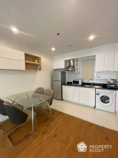 Modern kitchen with white cabinetry and stainless steel appliances, complemented by warm wooden flooring and a sleek dining area.