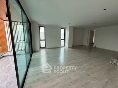 Spacious modern living room with large windows and balcony access, featuring sleek wooden flooring.