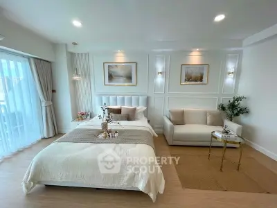 Luxurious bedroom with elegant decor and natural light, featuring a cozy seating area and stylish artwork.
